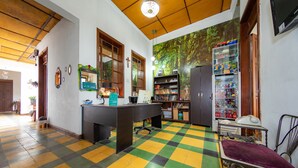 Ein Zimmer mit Schachbrettboden, einem Schreibtisch mit Computer, einem Bücherregal und einem Kühlschrank.