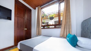 Ein Schlafzimmer mit einem Bett, einem an der Wand montierten Fernseher und einem Fenster mit Vorhängen.