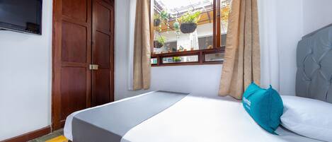 Un dormitorio con una cama, un televisor montado en la pared y una ventana con cortinas.