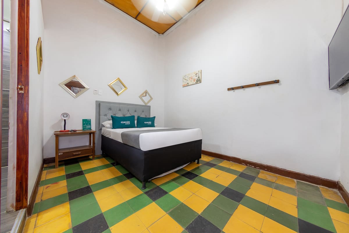Una habitación con cama, mesita de noche, espejo y televisor montado en la pared.