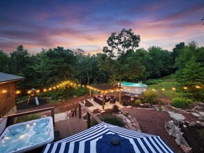 A backyard with a hot tub, a covered seating area, a swimming pool, and string lights.
