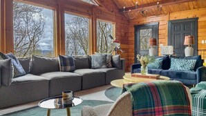 A cozy cabin interior with a large gray sofa, a round coffee table, and a plaid-covered chair. - Sky Pine Lodge - Chalet Atop the World (Jim Thorpe)