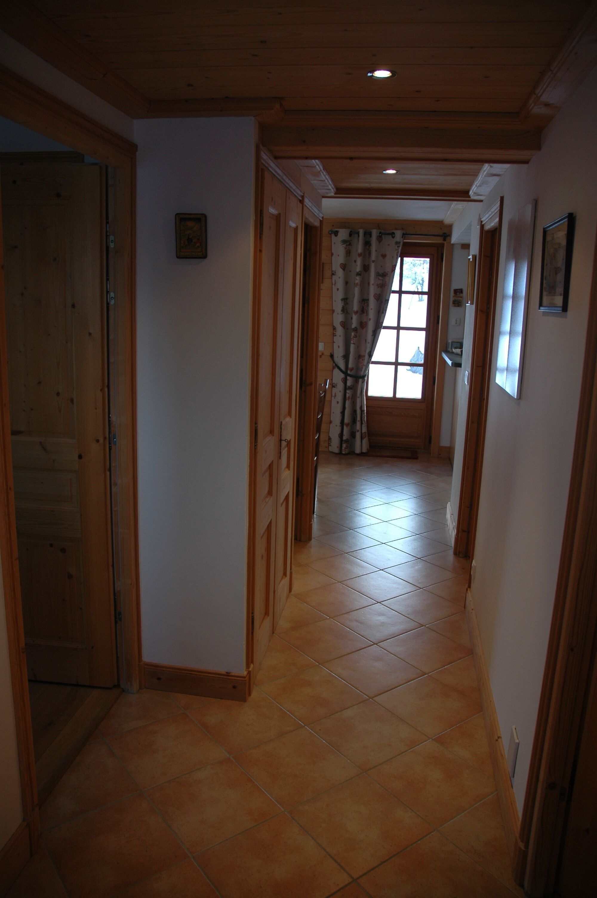 Un couloir avec des portes en bois, un sol carrelé et une fenêtre avec des rideaux.