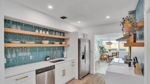 A modern kitchen with white cabinetry, a stainless steel refrigerator, and a teal backsplash. - Casa De Amigos | Private Pool | Outdoor Oasis (Fort Lauderdale)