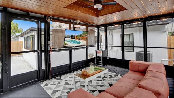 A spacious room with a wooden ceiling, large windows, a pool visible through the glass doors, and a modern sofa. - Casa De Amigos | Private Pool | Outdoor Oasis (Fort Lauderdale)