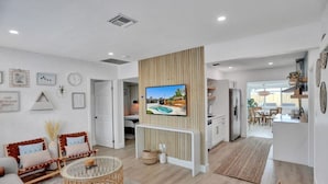 A modern living room with a TV, wicker furniture, and a dining area with a kitchen in the background. - Casa De Amigos | Private Pool | Outdoor Oasis (Fort Lauderdale)