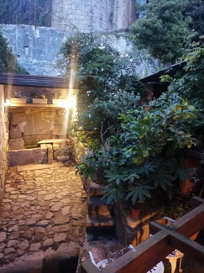 A stone courtyard with a bench, potted plants, and a small table.