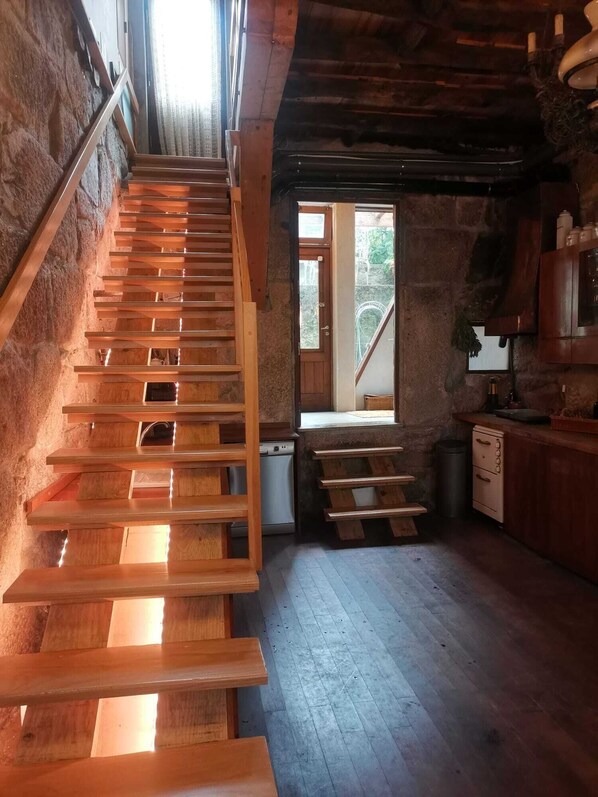 A rustic kitchen with wooden stairs leading to a loft area, a small sink, and a window providing natural light.