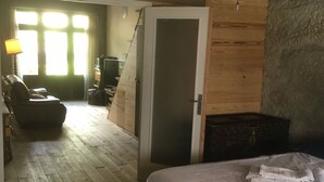 A bedroom with a wooden bed, a small desk, and a chair. There is a door leading to another room and a window with curtains. - Porto Old Downtown - Vérités Dame (Porto)