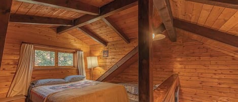 Ein gemütliches Schlafzimmer im Dachgeschoss mit Holzbalkendecke, einem Bett mit Quilt, einem Nachttisch und einem Fenster mit Vorhängen.