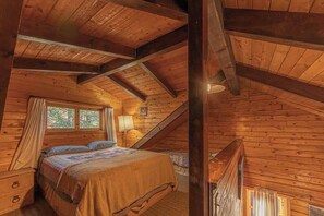 A cozy attic bedroom with a wooden ceiling, a bed with a quilt, a nightstand, and a window with curtains. - Forest Cabin 5 Old Glory (Payson)
