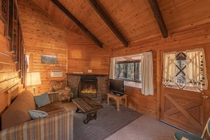 L’intérieur d’un chalet confortable, avec une cheminée, un téléviseur et un canapé en osier.