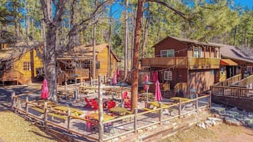 A rustic cabin with a deck, outdoor seating, and a large tree in the foreground.