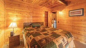 A wooden cabin room with a bed, a nightstand, a lamp, and a framed American flag on the wall. - Forest Cabin 5 Old Glory (Payson)