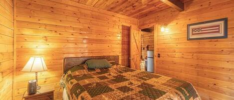 Une chambre rustique en bois, avec un lit, une table de chevet, une lampe et un drapeau américain encadré accroché au mur.