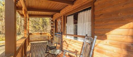 Een houten vakantiehuis met een veranda, twee metalen stoelen en een kleine tafel.