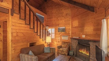 A cozy log cabin interior with a fireplace, wooden walls, a sofa, and a chair.