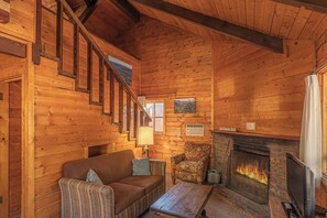 A cozy log cabin interior with a fireplace, wooden walls, a sofa, and a chair. - Forest Cabin 5 Old Glory (Payson)