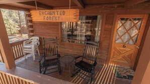 Une cabane en bois avec une pancarte indiquant « FORÊT ENCHANTEE », une porte portant le numéro « 6 », et deux chaises ainsi qu’une petite table sur le porche.