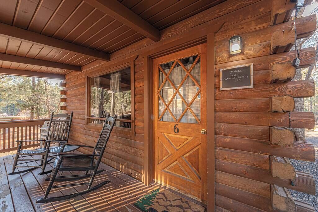 Eine Blockhütte mit einer Holztür, auf der '6' steht, Schaukelstühle auf der Veranda und einem Schild mit einer Internetadresse.