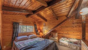 Une cabane chaleureuse avec un intérieur en bois, un lit recouvert d’une courtepointe, une chaise et une petite table avec une lampe.