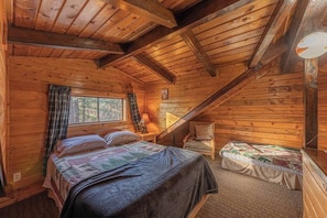 A cozy cabin with a wooden interior, a bed with a quilt, a chair, and a small table with a lamp.