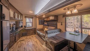 A compact RV interior with a kitchenette, seating area, and a table.