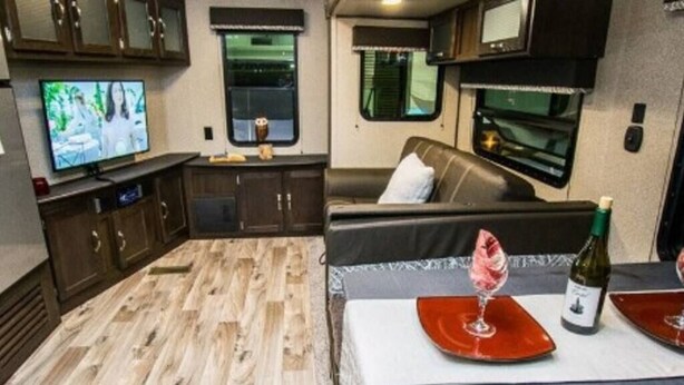 A compact RV interior with a dining area, a sofa, a television, and a kitchenette.