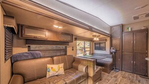 A compact RV interior with a leather sofa, a small dining table, and a kitchenette area.