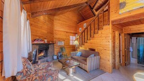 A cozy log cabin interior with a fireplace, wooden walls, a sofa, a coffee table, and a staircase.
