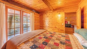 A wooden cabin bedroom with a large bed, a window with curtains, and a small kitchenette area.