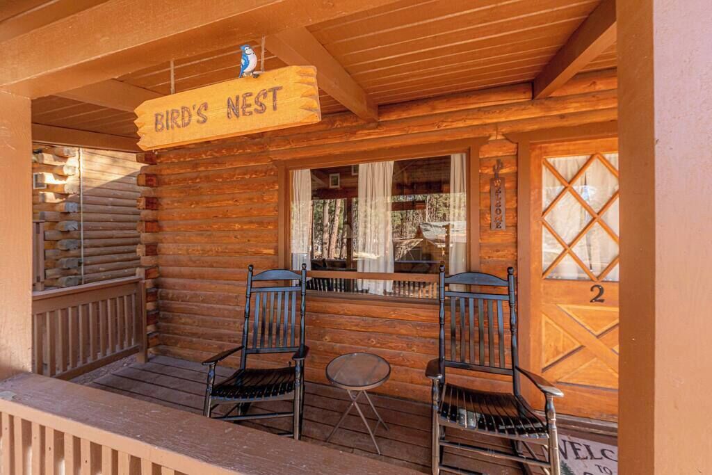 A wooden log cabin with a porch, two chairs, a small table, and a sign reading "Bird's Nest".