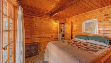 A wooden cabin bedroom with a bed, a dresser, and a window with curtains.