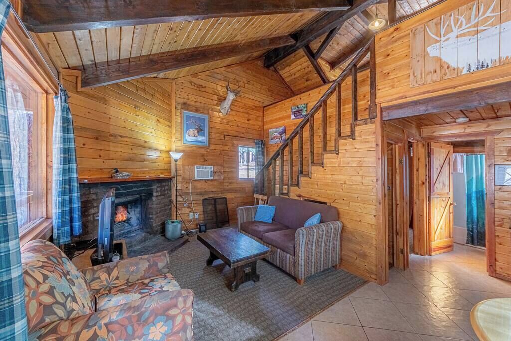 L’intérieur d’un chalet confortable, avec une cheminée, des murs en bois, un canapé et un escalier.