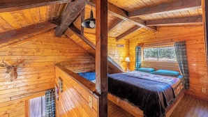 Une chambre dans un chalet en rondins, avec un lit en mezzanine, des murs en bois, une décoration représentant une tête de cerf et une fenêtre avec des rideaux.