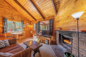 A cozy cabin interior with a fireplace, wooden walls, a television, and a dining area. - Forest Cabin 1 Hunters Blind (Payson)