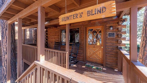 A wooden cabin with a porch, a sign reading "Hunter's Blind," and a wooden door with a window. - Forest Cabin 1 Hunters Blind (Payson)