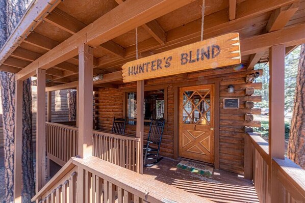 A wooden cabin with a porch, a sign reading "Hunter's Blind," and a wooden door with a window. - Forest Cabin 1 Hunters Blind (Payson)