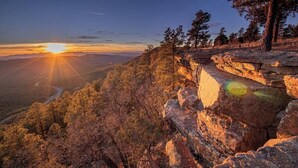 Une falaise rocheuse offrant une vue imprenable sur le coucher de soleil, avec des arbres et une route sinueuse en contrebas.