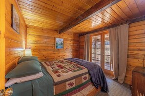 A wooden cabin room with a bed, a window, and a door.