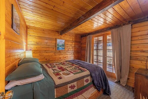 Une pièce en bois, aménagée comme une cabane, avec un lit, une fenêtre et une porte.