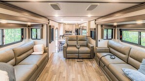 Interior espacioso de una casa rodante con sofás de cuero, una zona de comedor central y ventanas amplias.