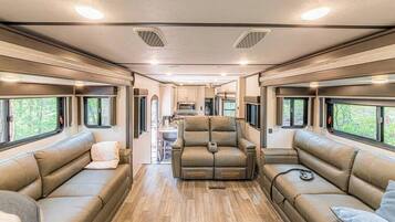Interior espacioso de una casa rodante con sofás de cuero, una zona de comedor central y ventanas amplias.