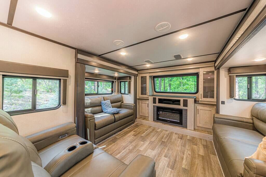 Interior moderno de una caravana recreativa, con una zona de estar acogedora, una unidad de entretenimiento integrada y grandes ventanales que ofrecen vistas al exterior.