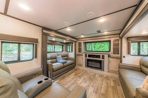 Een modern RV-interieur met een gezellige zithoek, een ingebouwde entertainmentsunit en grote ramen met uitzicht op de natuur.