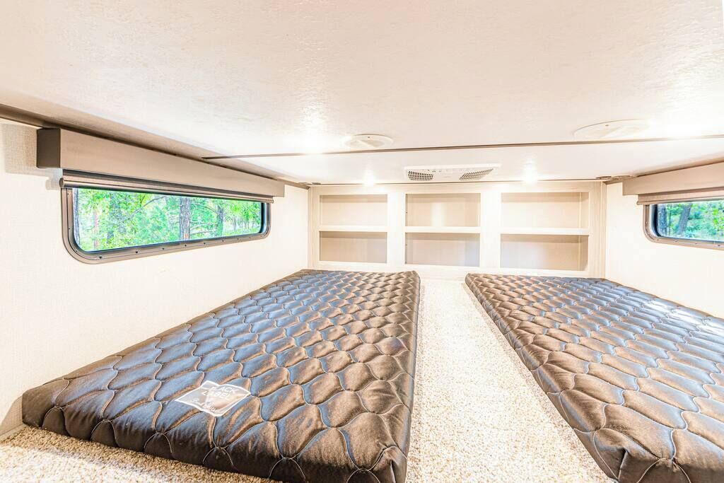 Interior compacto de una autocaravana con dos camas, un pasillo central y ventanas que dan a zonas verdes.