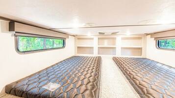 Interior compacto de una autocaravana con dos camas, un pasillo central y ventanas que dan a zonas verdes.