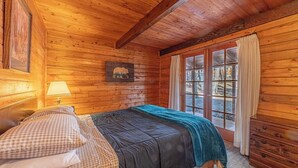 Een slaapkamer in een houten hutje, met een bed, een raam met gordijnen en een beren afbeelding aan de muur.