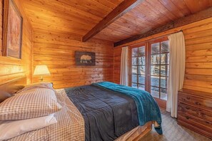 Un dormitorio de cabaña de madera con una cama, una ventana con cortinas y un cuadro de un oso en la pared.