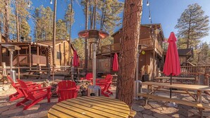 A rustic wooden cabin with outdoor seating, including red chairs and picnic tables, surrounded by trees. - Forest Cabin 3 Bear's Den (Payson)